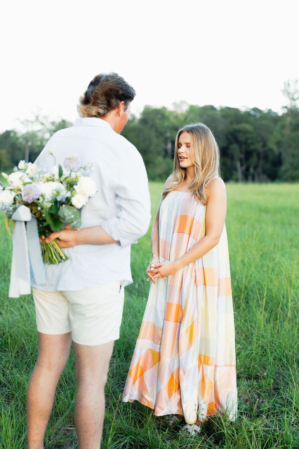 A couple stands in a green field during an intimate pregnancy announcement.