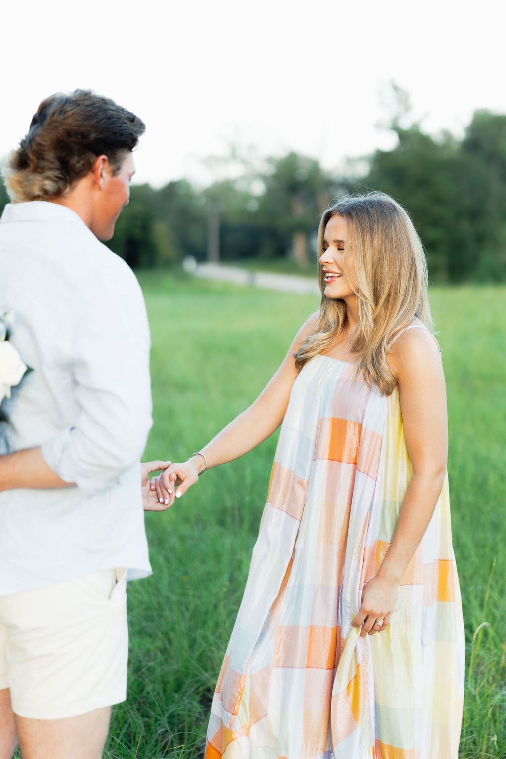Gender reveal photo ideas: Couple standing in a field with the groom holding the gender reveal flowers behind his back before they do the gender reveal