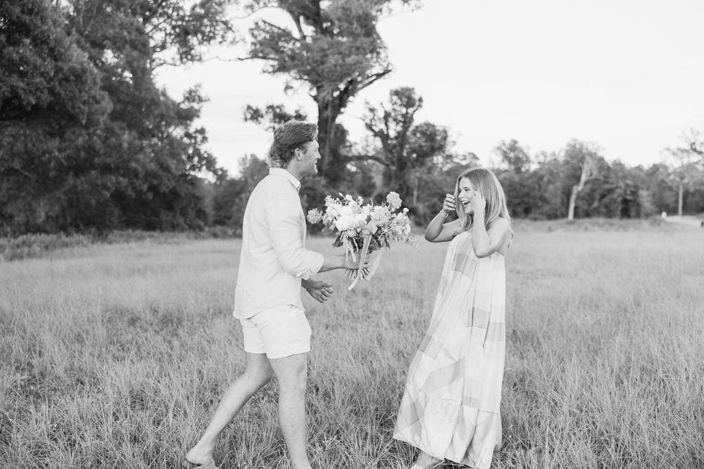 A black and white photo of a couple revealing their baby's gender with a floral arrangement.