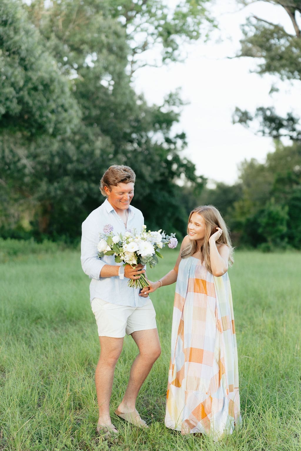 Couple holding hands in a field and smiling at the floral bouquet during their gender reveal photos.
