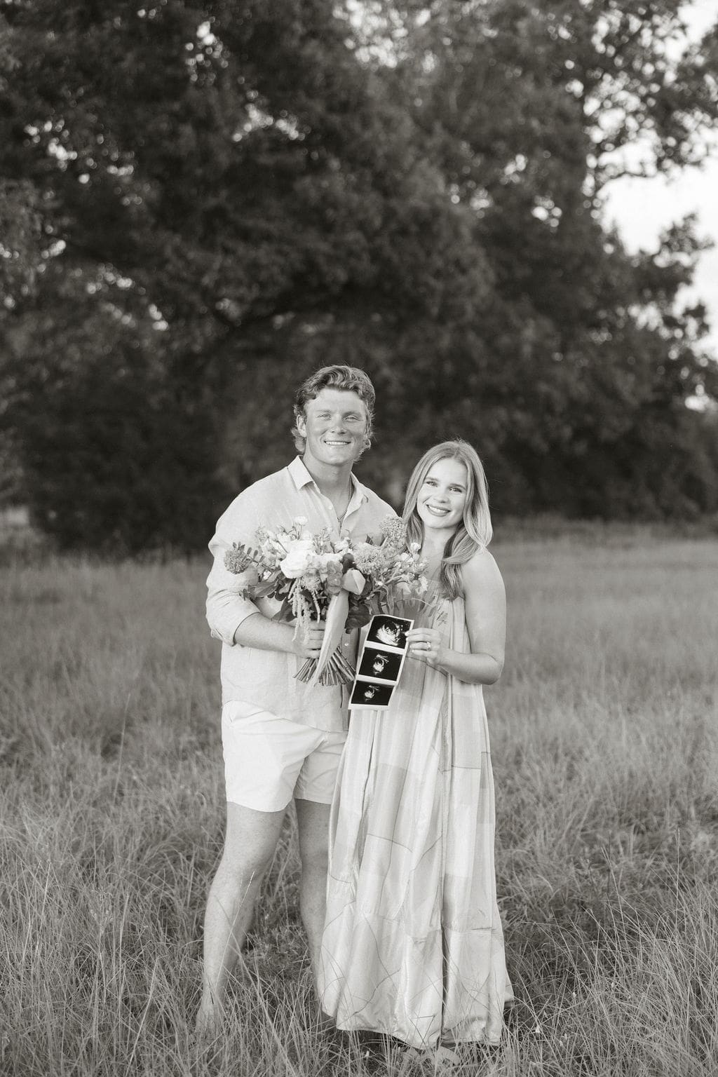 A black and white photo of a couple holding a floral bouquet and the ultrasound photos during their gender reveal photoshoot.