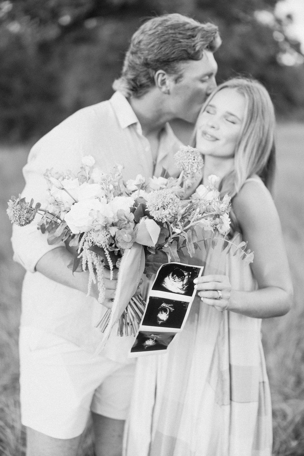 A closeup of a husband kissing his wifes forehead during their gender reveal photoshoot.