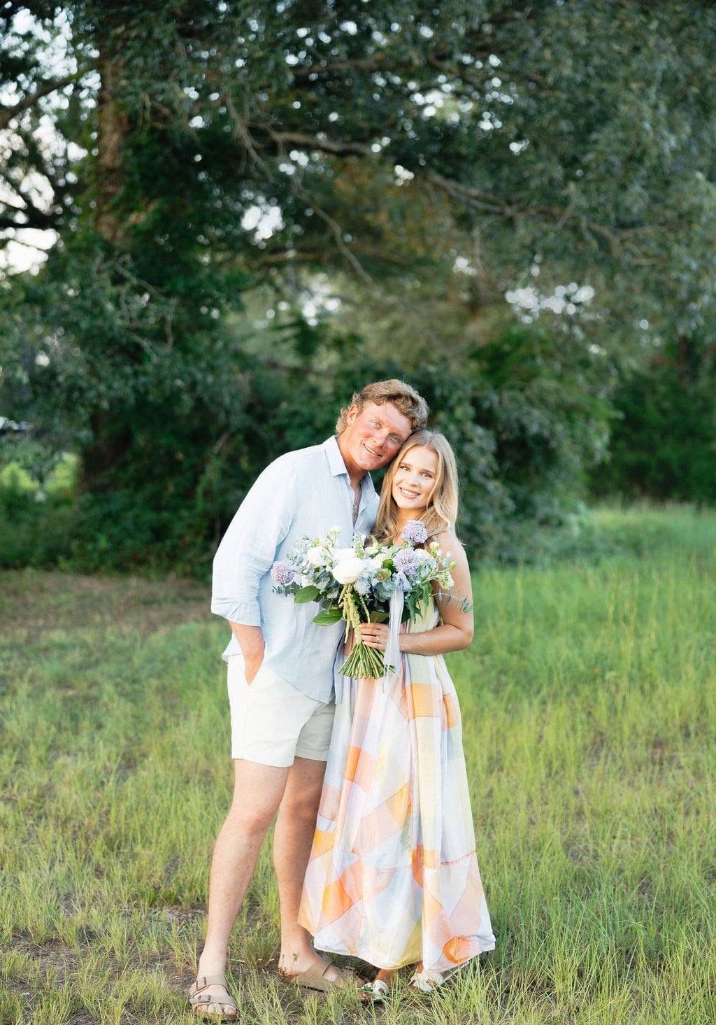 A couple stands in a green field during an intimate pregnancy announcement.