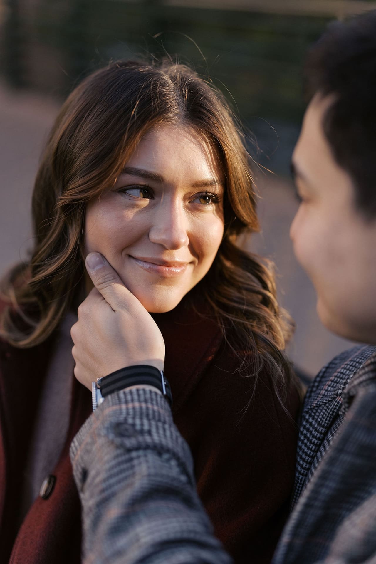 A closeup of a man holding his fiances cheek as she smiles up at him with the sun shining on her face.