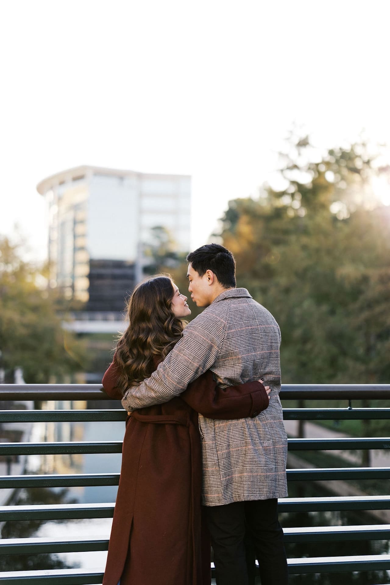 A couple standing next to each other hugging with the sunrise shining through the trees. Romantic Engagement Photo Ideas
