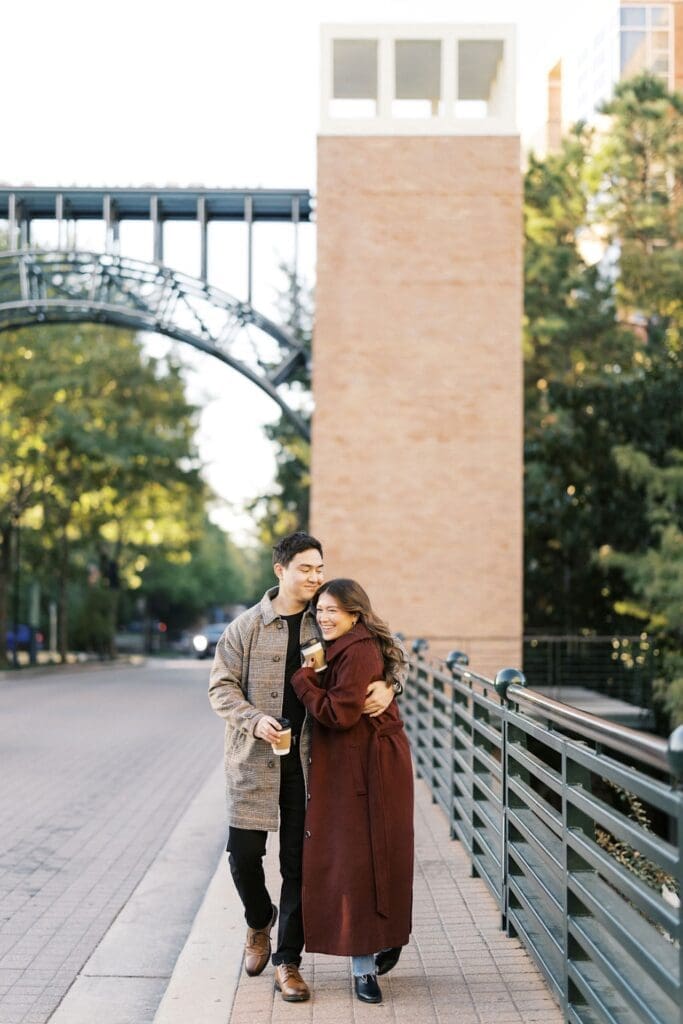 Romantic Engagement Photo Ideas: Couple walking and hugging as they cross a bridge during their engagement shoot,