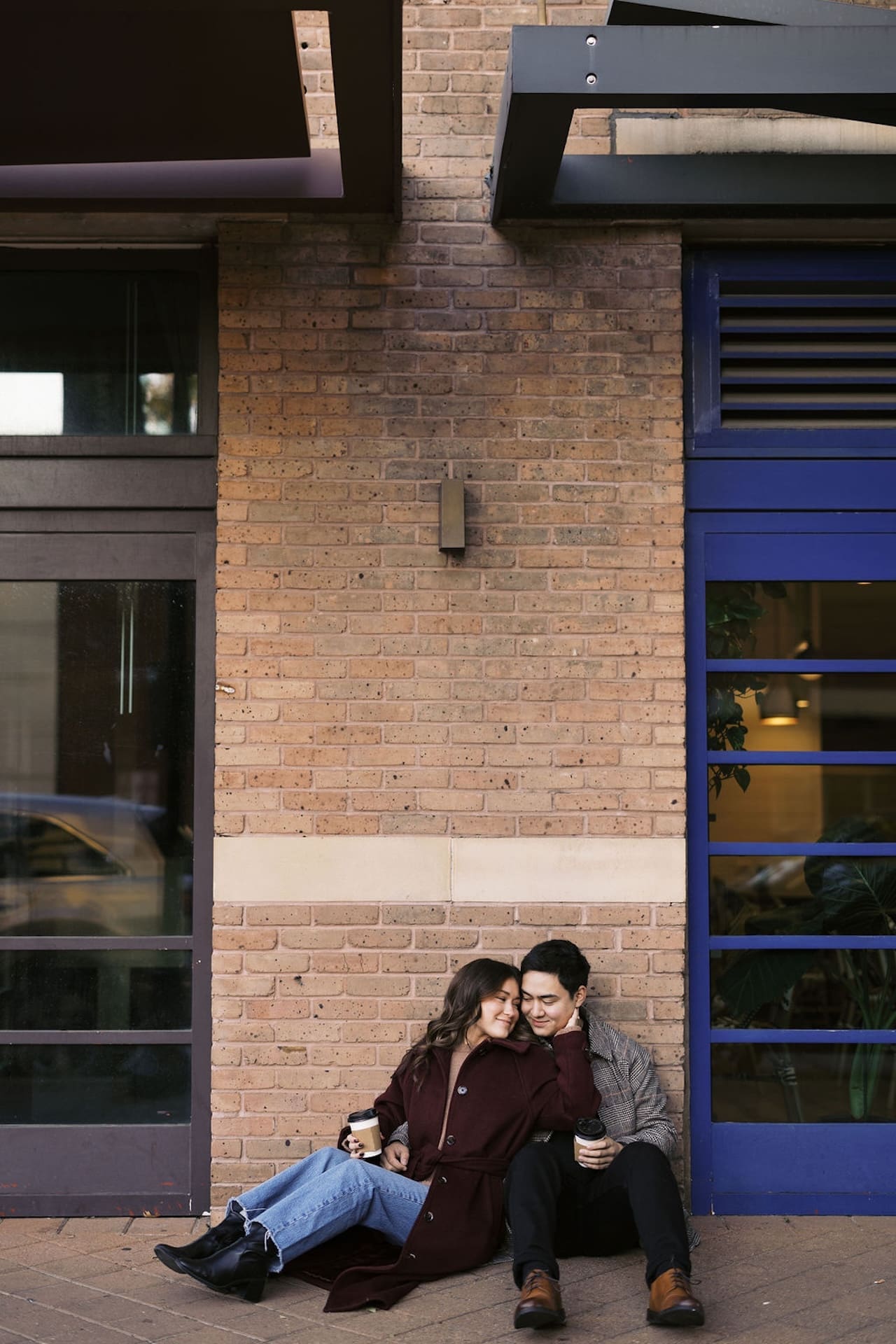 A couple sitting on the ground in front of a coffee shop showcasing Romantic Engagement Photo Ideas