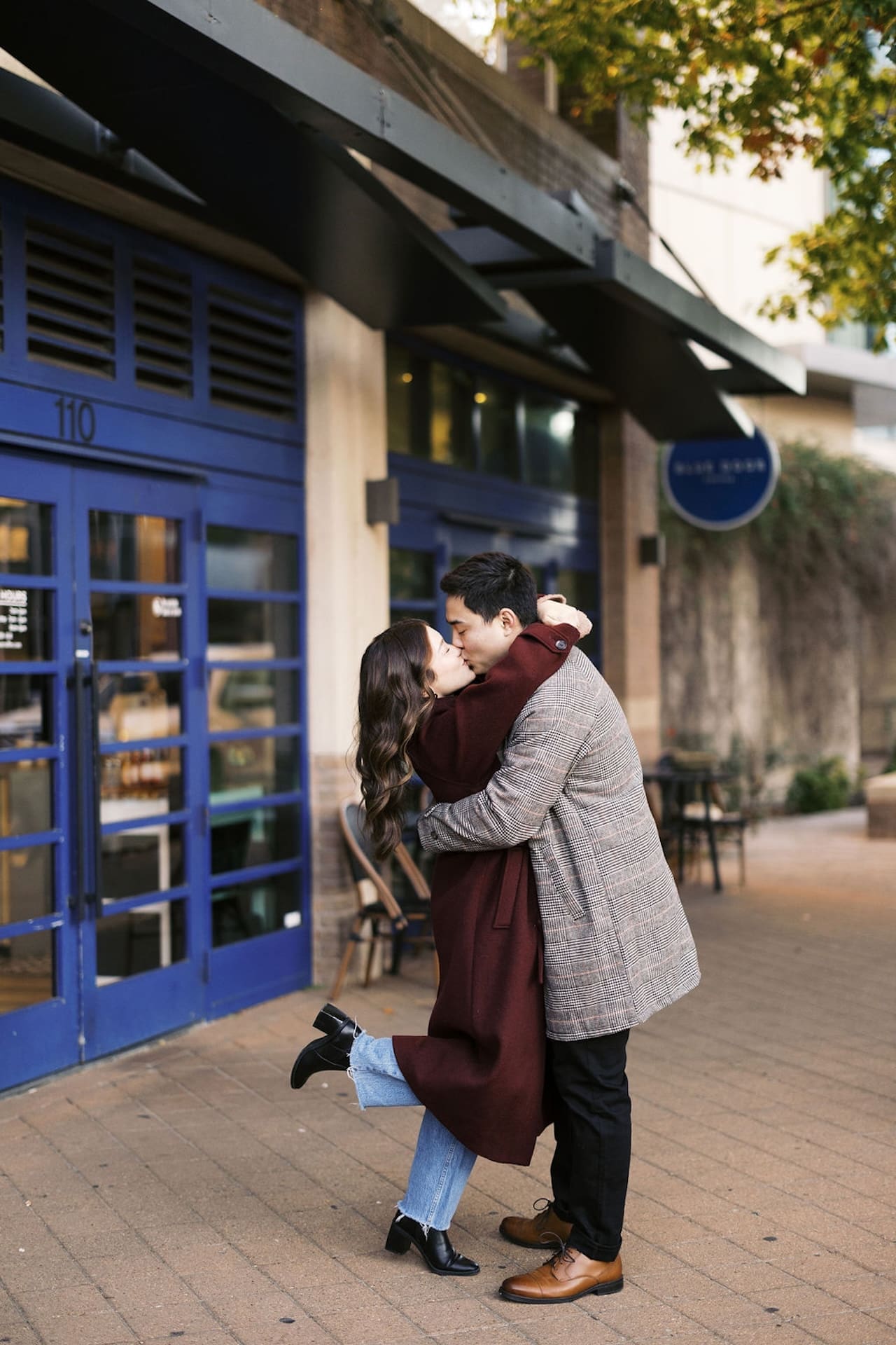 Romantic Engagement Photo Ideas: Engaged couple hugging and kissing in front of a coffee shop during their sunrise engagement shoot,