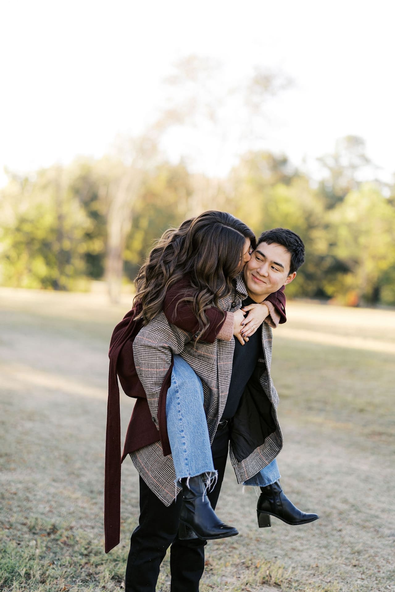 Romantic Engagement Photo Ideas: A couple doing a piggy back in a field while they smile and laugh together.