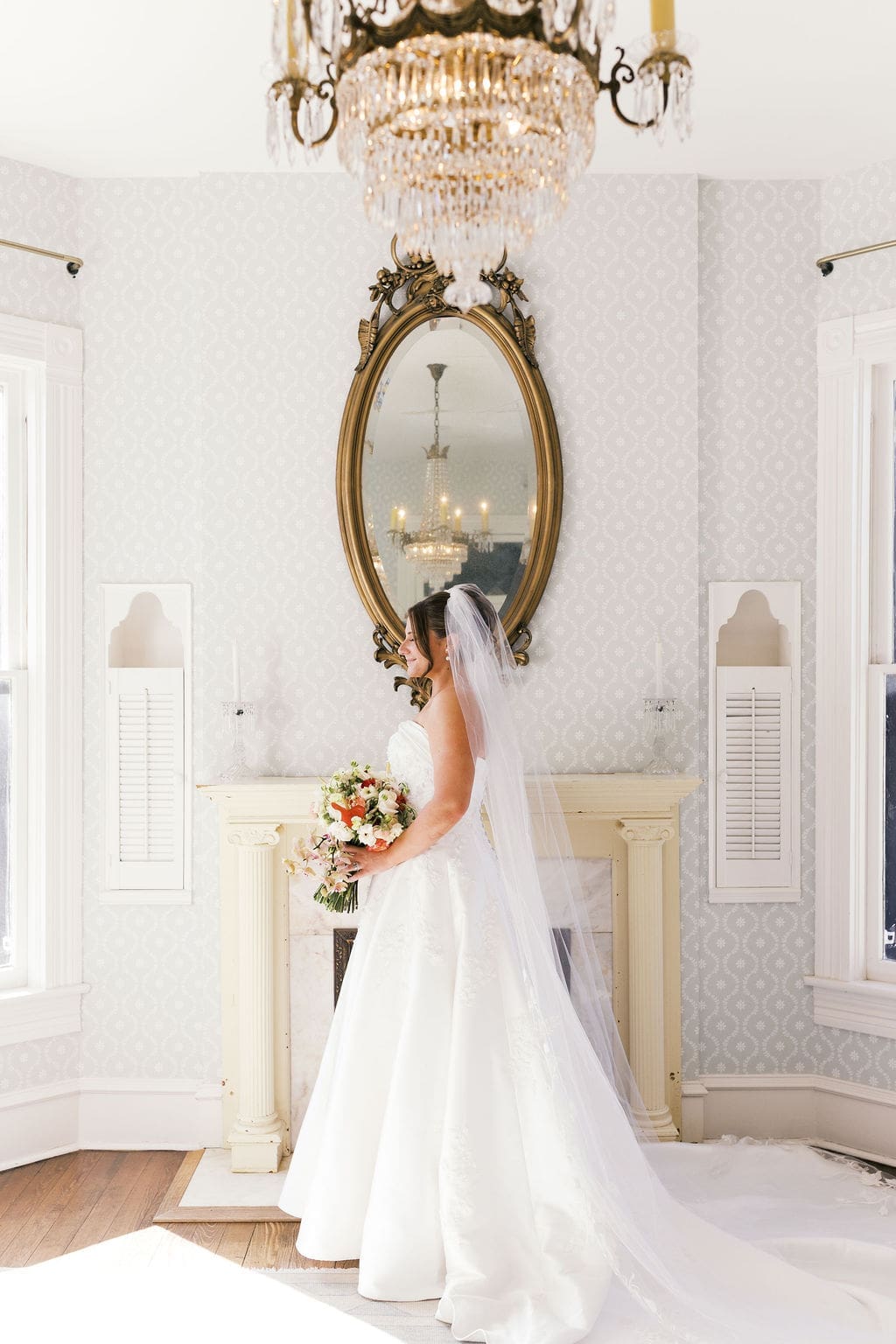 A beautiful bridal photo of the bride smiling softly while holding her wedding bouquet and looking out the window at woodbine mansion.