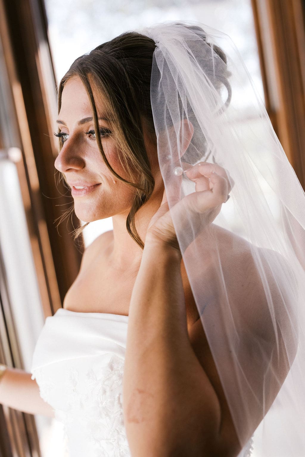 The bride adjusting her earing as she looks out the window at Woodbine Mansion during her bridal portraits.