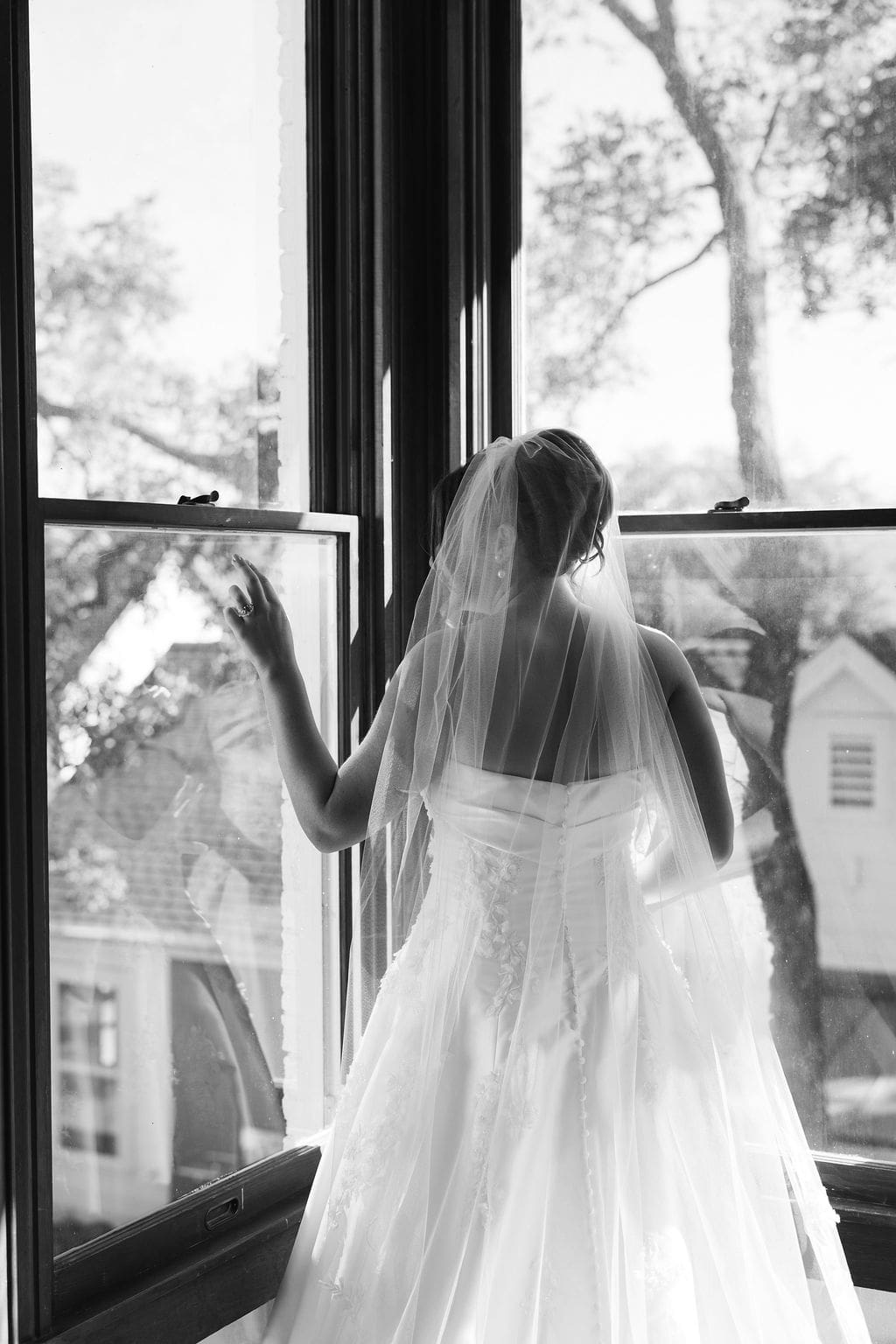 A black and white photo of a bride looking out the window during her bridal portraits.