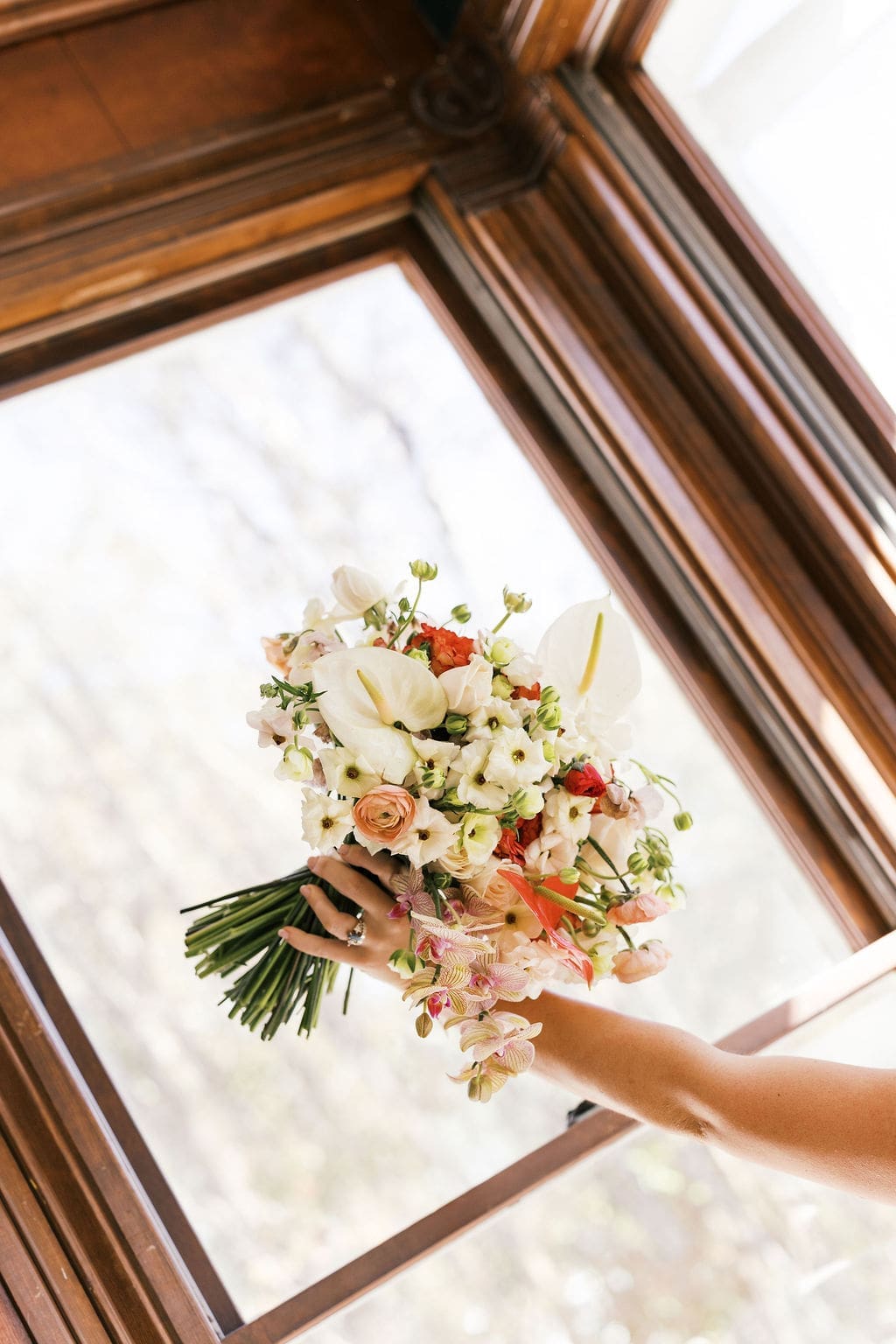 An editorial of the bride holding her wedding bouquet in the air in the window at Woodbine Mansion