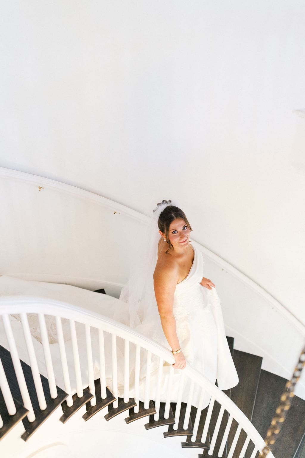 Bride looking up at the photographer smiling softly as she walks down an elegant staircase for her bridal portraits.