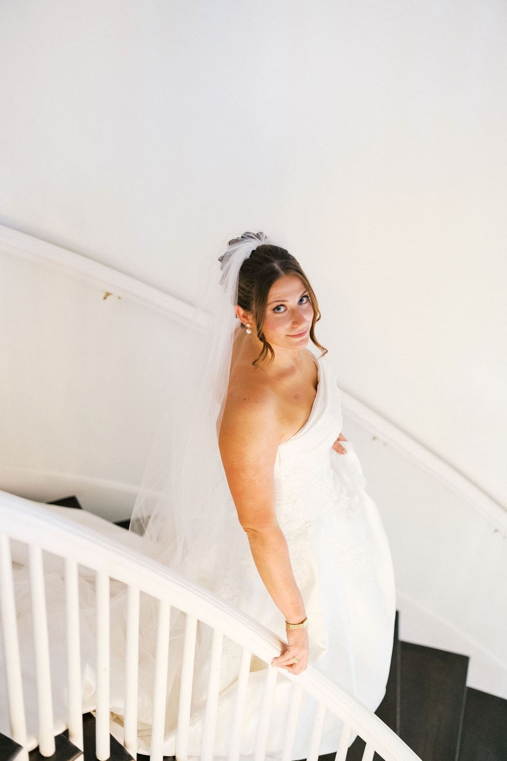 Bride looking up at the photographer smiling softly as she walks down an elegant staircase for her bridal portraits.
