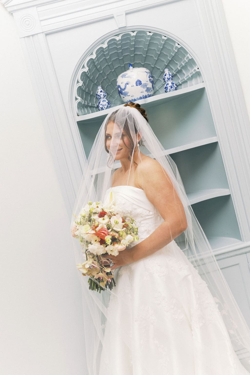 The bride smiling softly in the distance with her veil draped over her for a unique bridal portrait.
