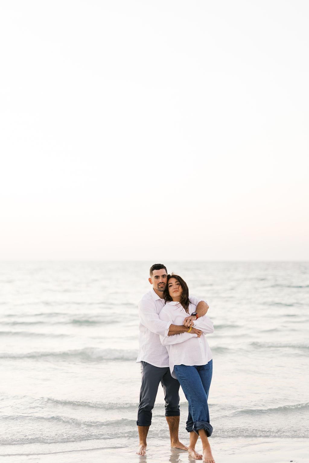 Couple hugging in the ocean at the beach after their destination elopement, wearing casual outfits and standing in the water.