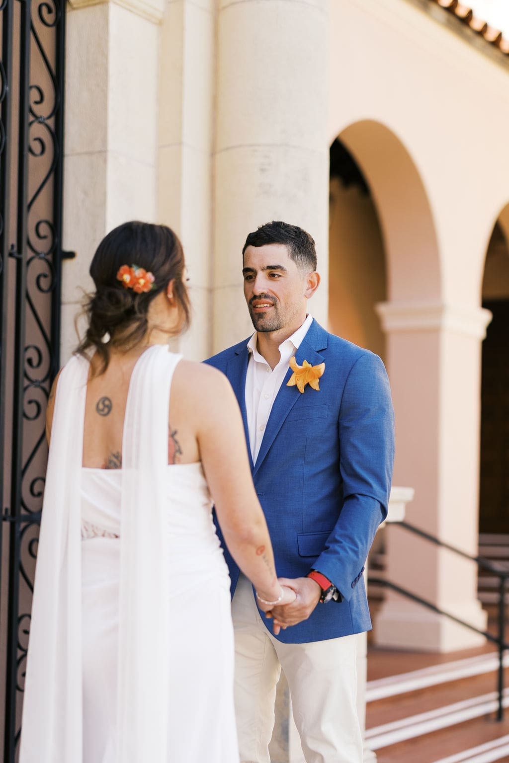 Groom holding the bride’s hands and looking at her during their destination elopement ceremony outside a historic courthouse with architectural arches.