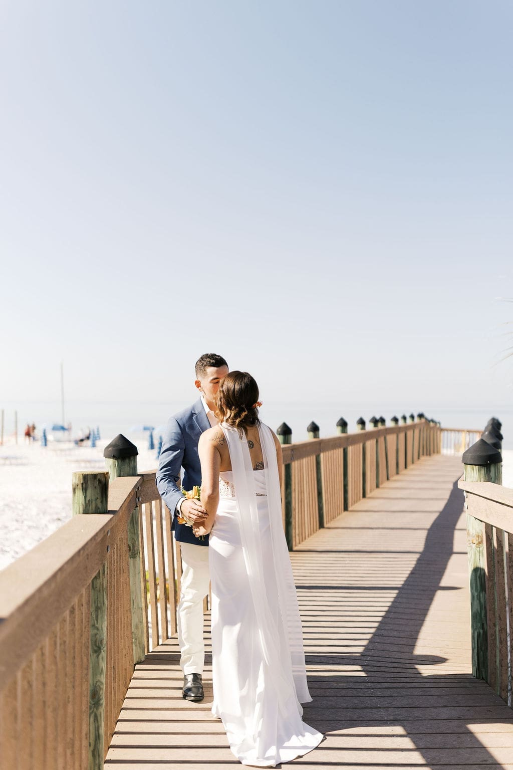 Couple kissing on a wooden beach boardwalk during an intimate destination elopement, with the ocean and white sand in the background.