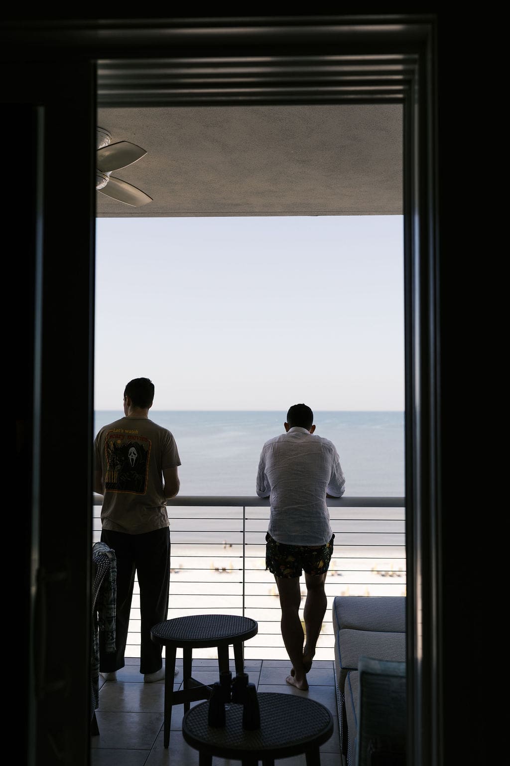 Groom and his best man standing on a balcony looking out over the beach and ocean in the morning light before an intimate elopement day.