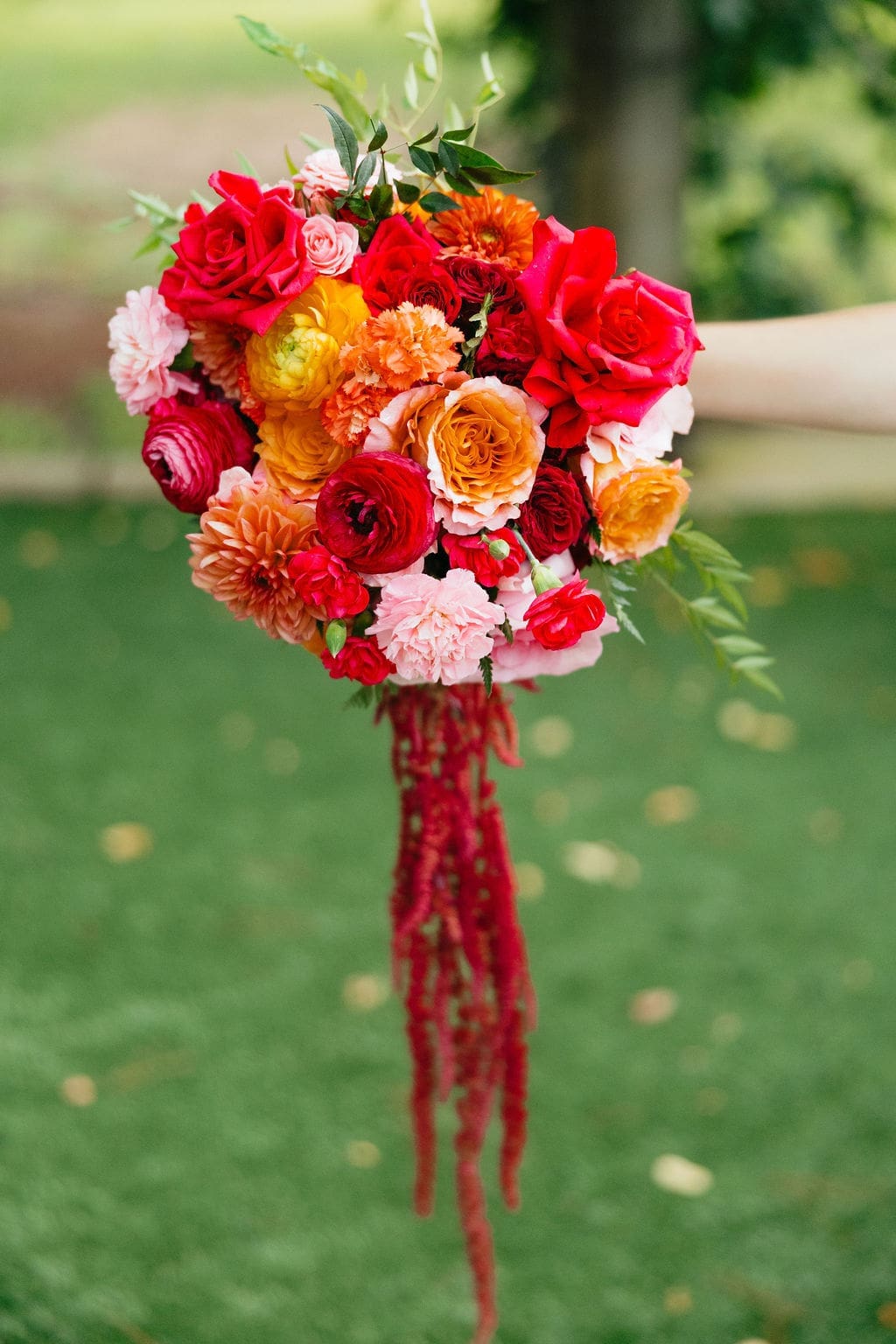 A detail photo of the brides vibrant orange and pink bridal bouquet, as she holds it over the grass to capture the details.