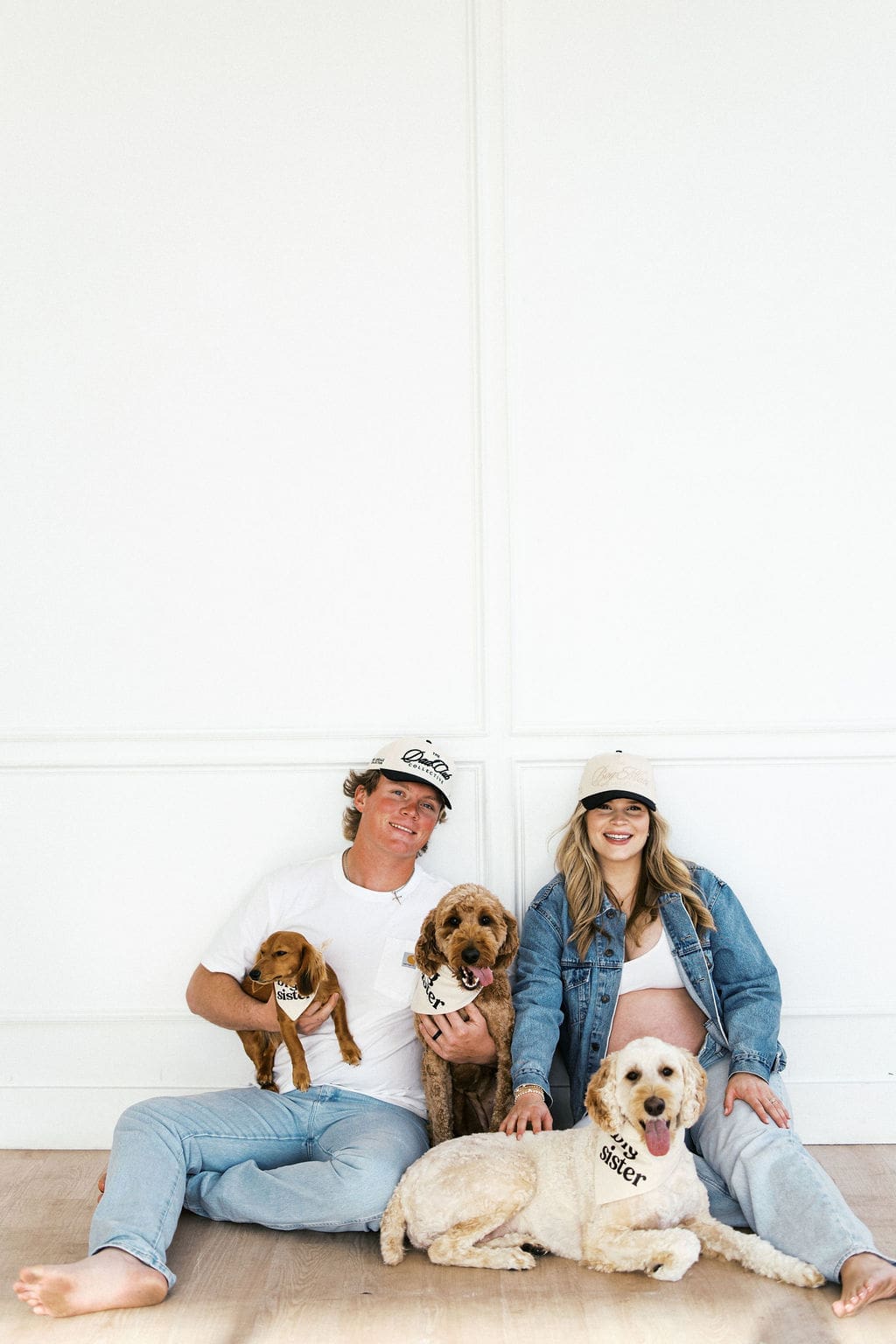 Candid studio maternity photos of the couple sitting on the floor on the studio with their dogs playing around them.