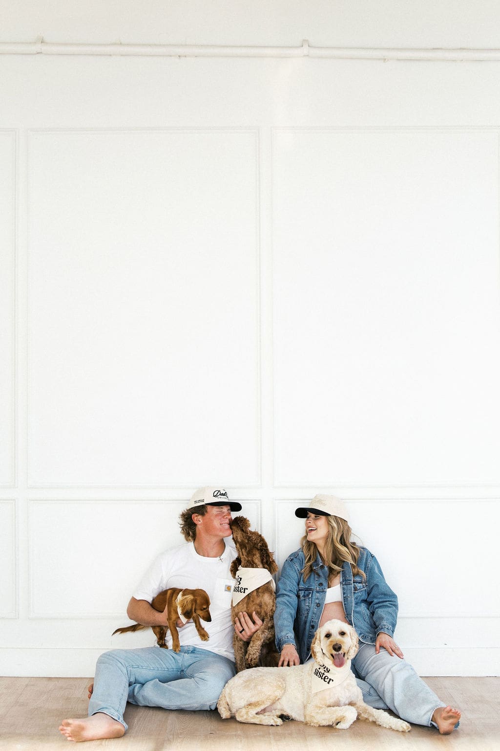 Candid studio maternity photos of the couple sitting on the floor on the studio with their dogs playing around them.