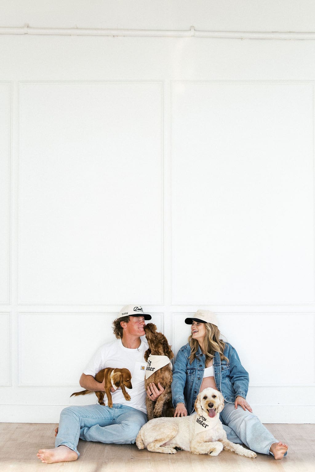 Candid studio maternity photos of the couple sitting on the floor on the studio with their dogs playing around them.