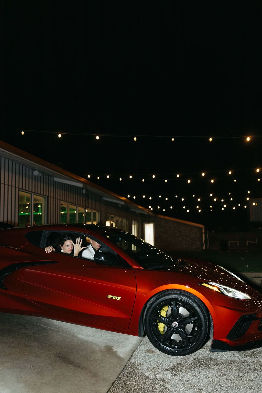 A fun documentary wedding photo of the bride and groom leaving their wedding venue in a bright red corvette.