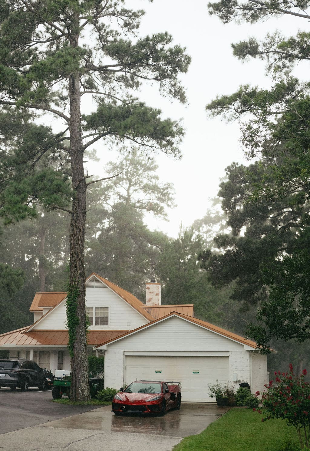 Rain falls around a white house with a copper roof and a red sports car in the driveway, part of the honest storytelling style seen in documentary wedding photos.