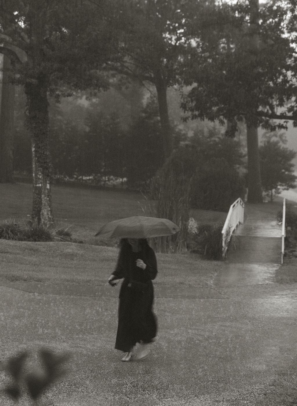 Black and white image of a woman walking through heavy rain with an umbrella outside the venue, creating a moody, cinematic moment before the ceremony.
