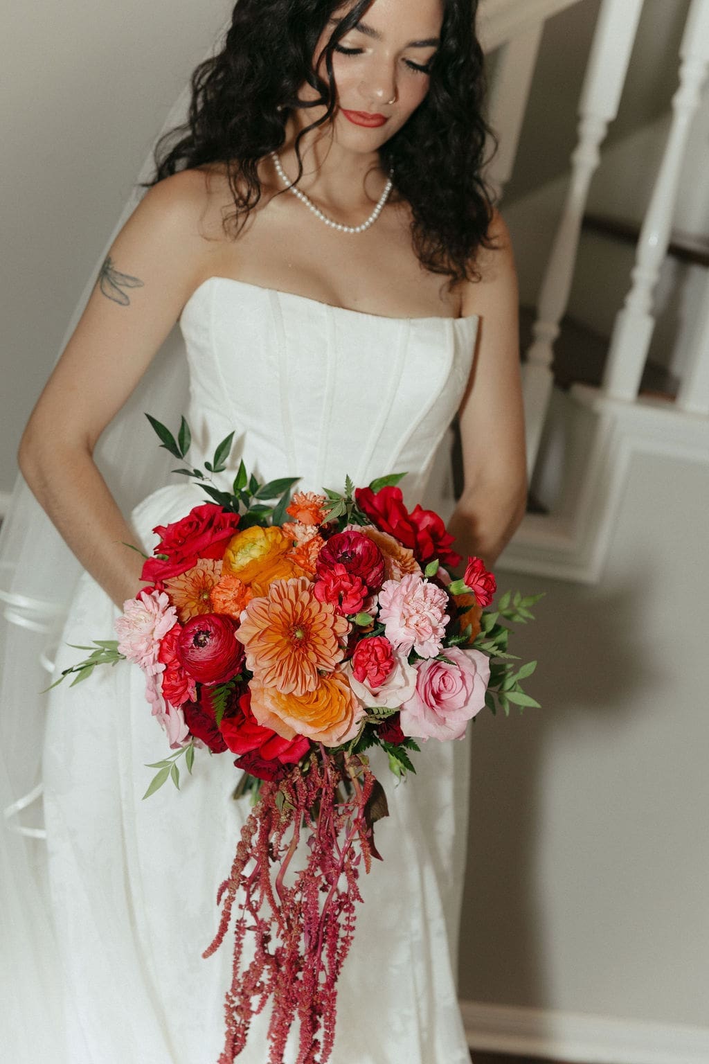 An editorial bride photo of the bride looking down at her vibrant pink and orange wedding bouquet.