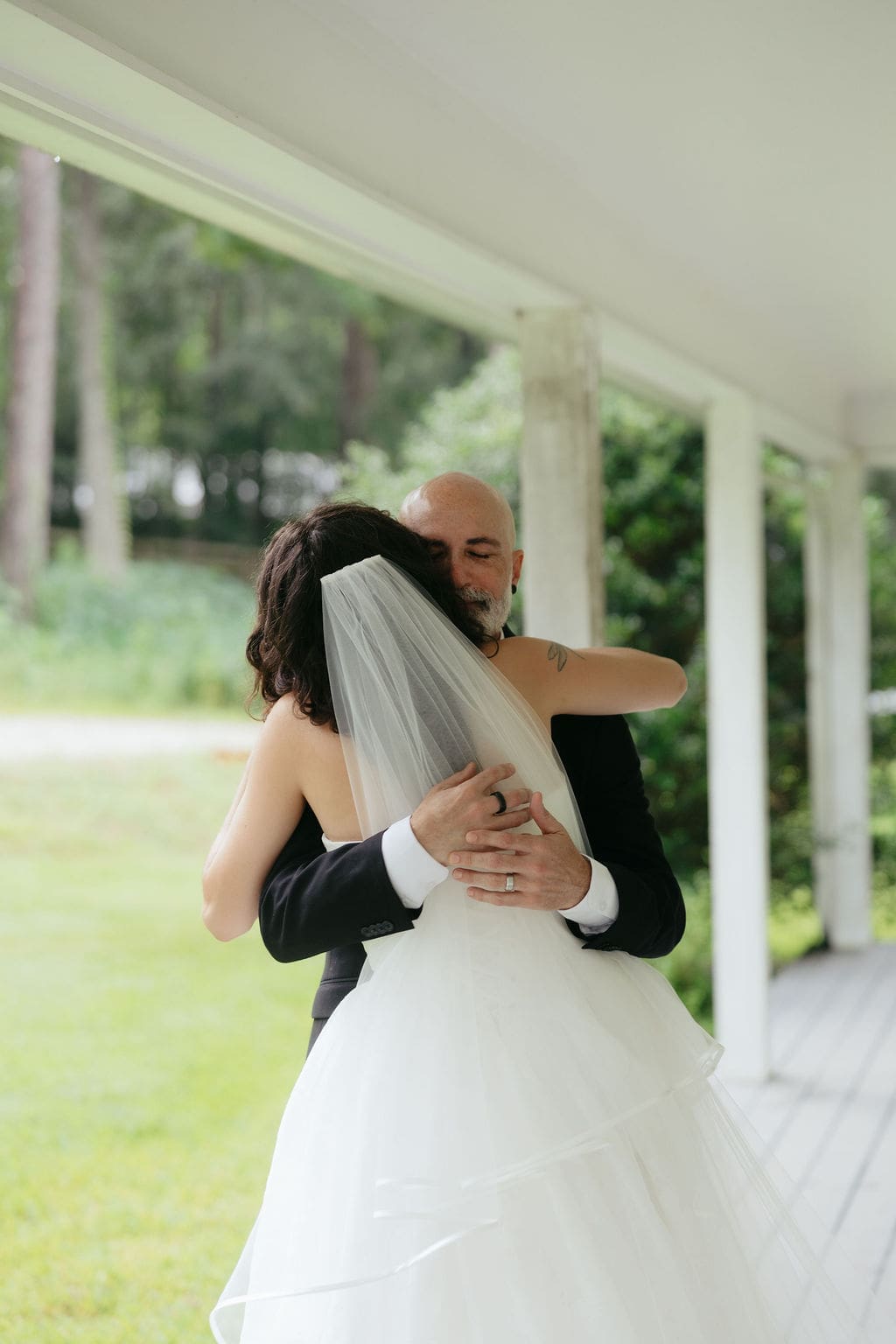 Bride hugs an her dad tightly on the porch, veil cascading down her back, a heartfelt embrace preserved in documentary wedding photos.