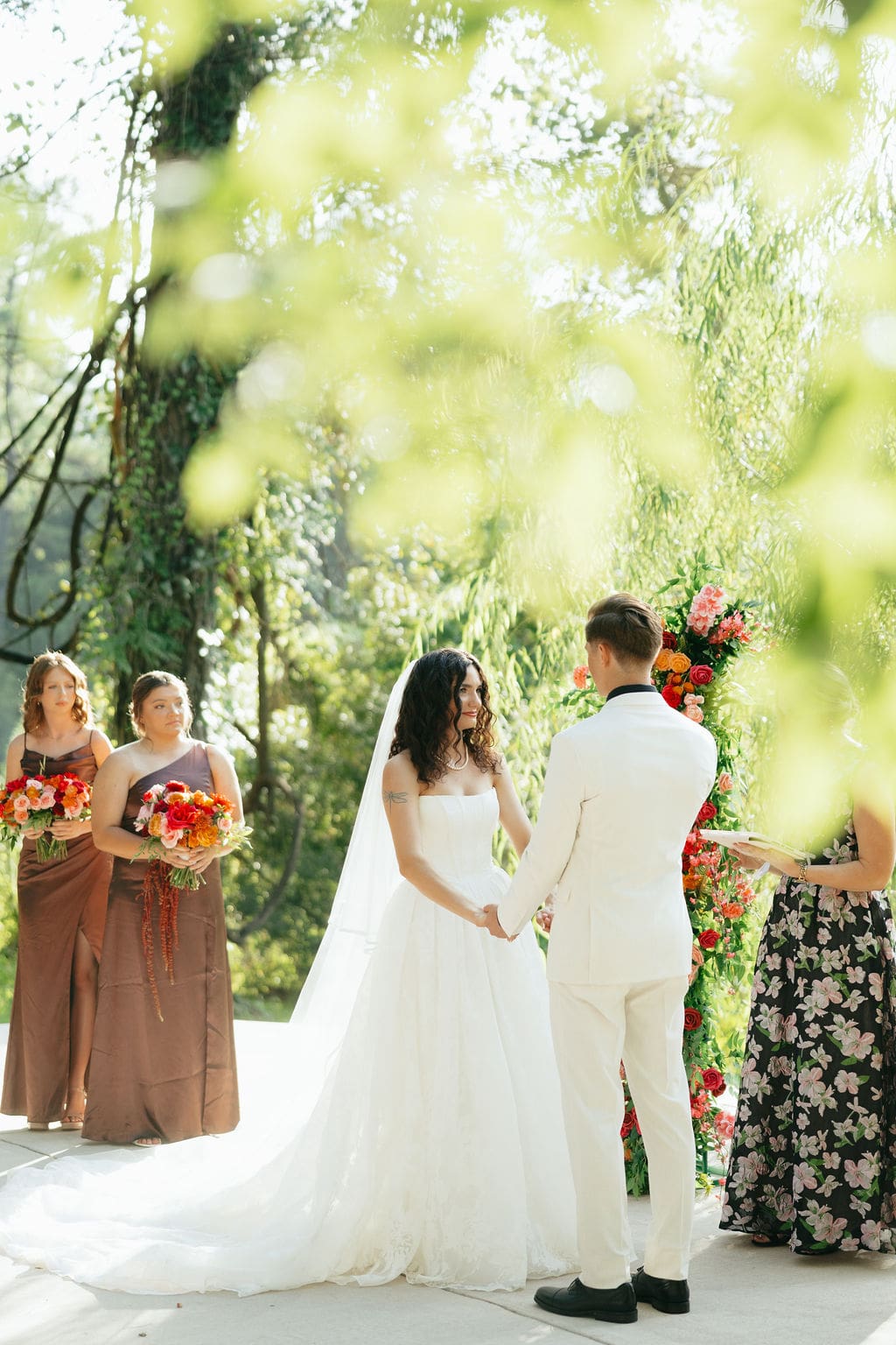 The bride and groom holding hands at the alter, with the bridesmaids in brown dresses in a line behind the bride.