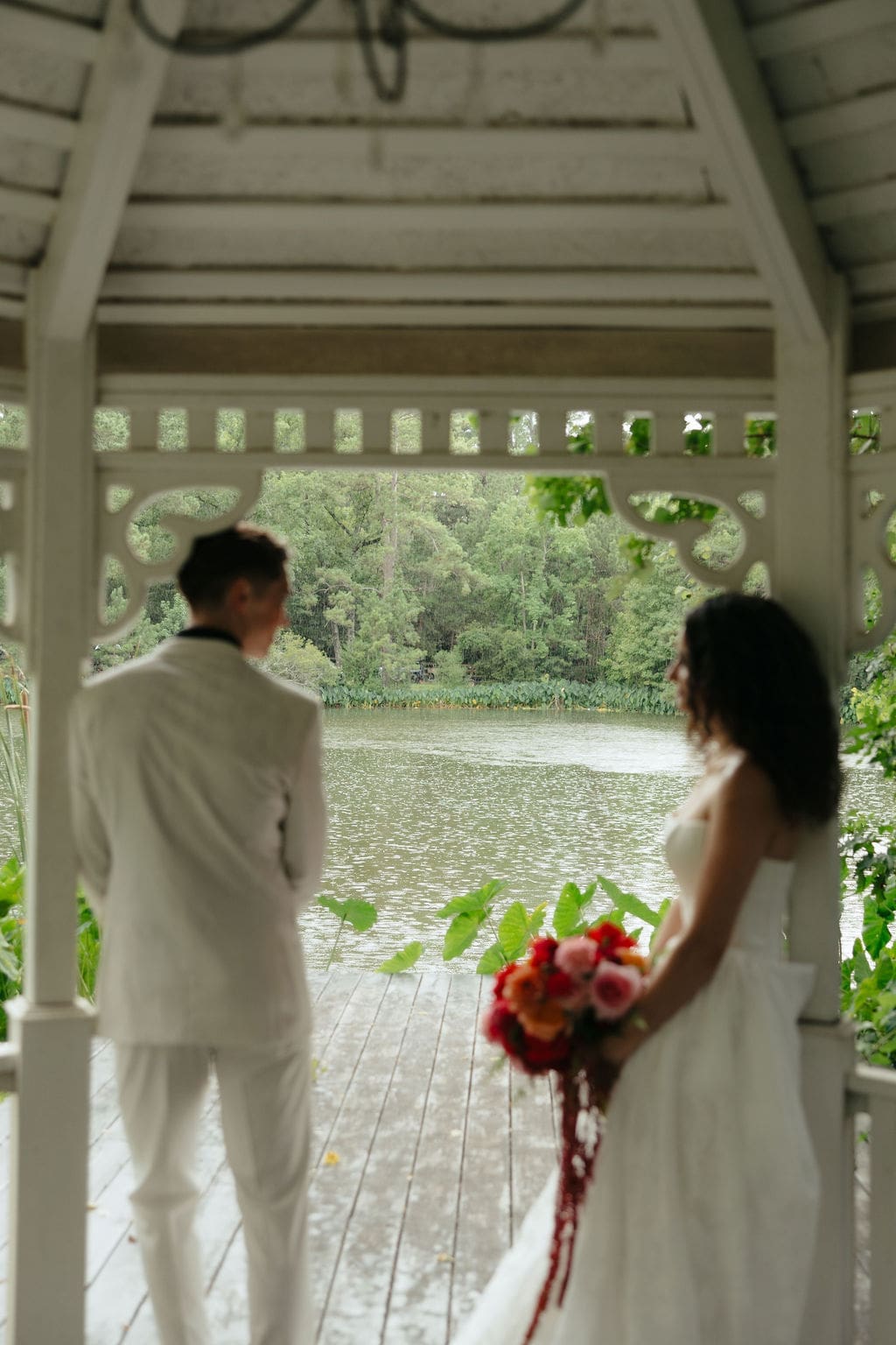 A candid wedding photo of the bride and groom standing under a pavilion by a pond while it was pouring rain during the wedding portraits.
