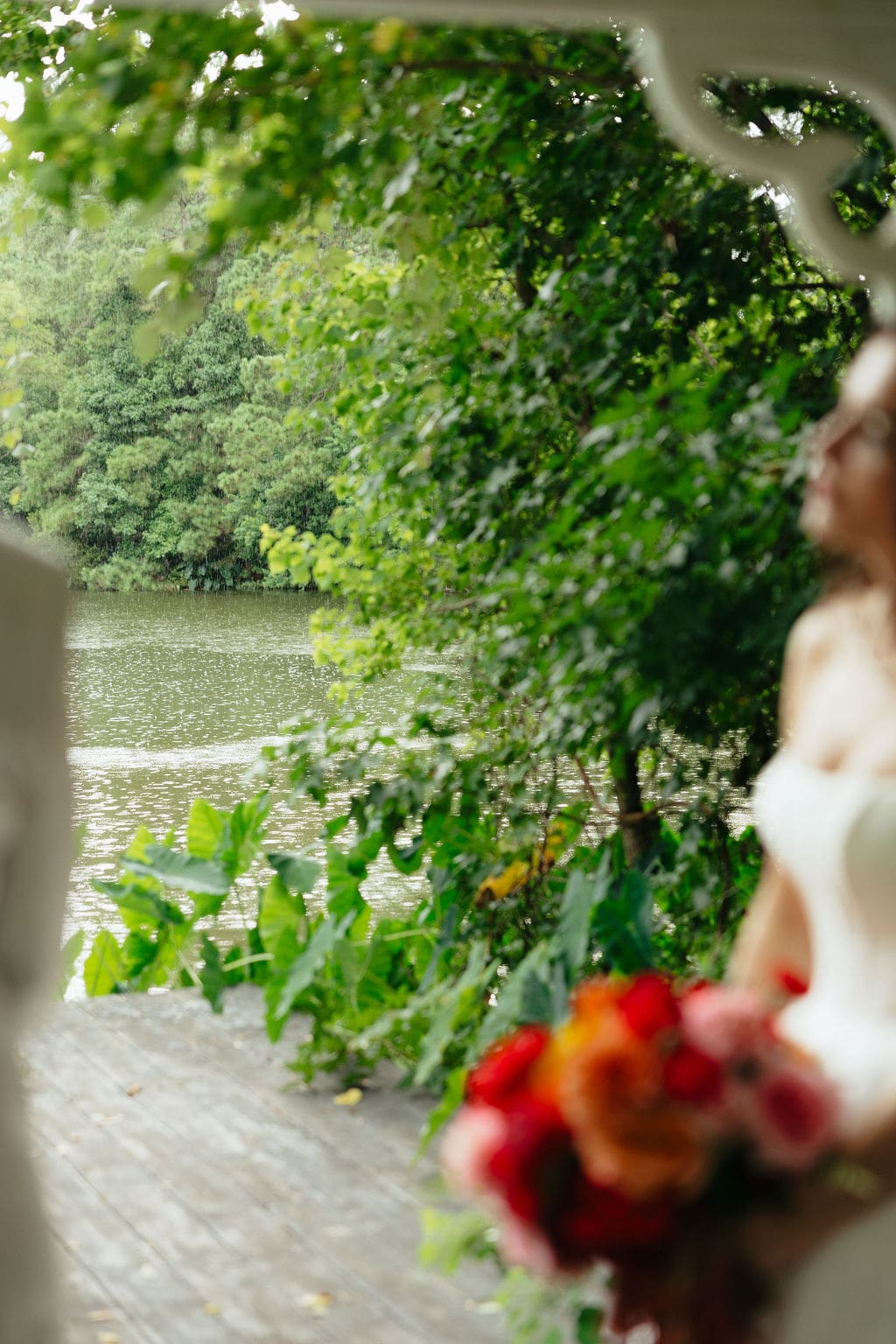 A detail photo of a blurred out bride leaning against the pavillion holding her vibrant wedding florals, an amazing example of documentary wedding photos.