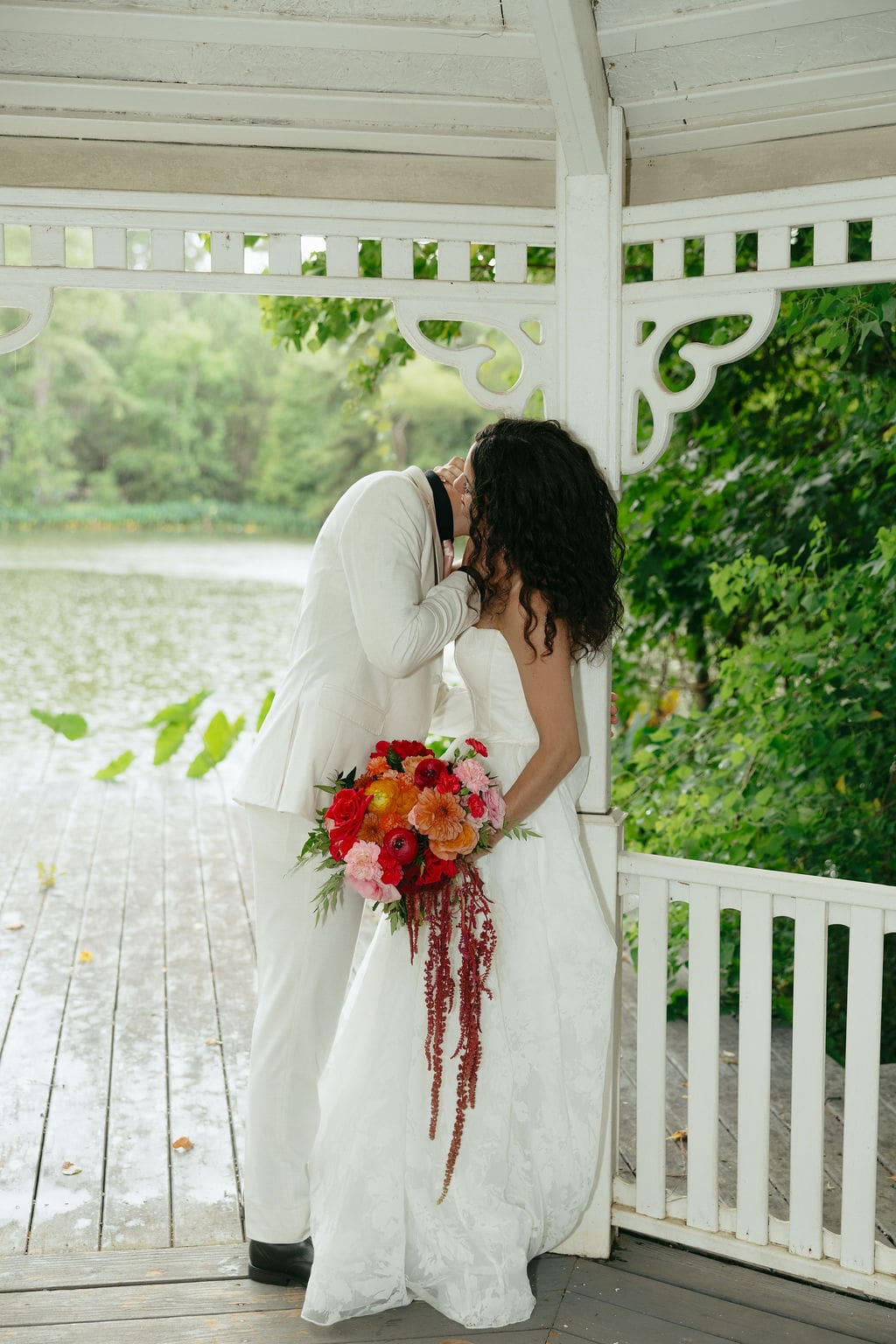 Timeless documentary wedding photos of the bride and groom standing under a pavillion with the groom leaning in to kiss his wife as the rain falls behind them.