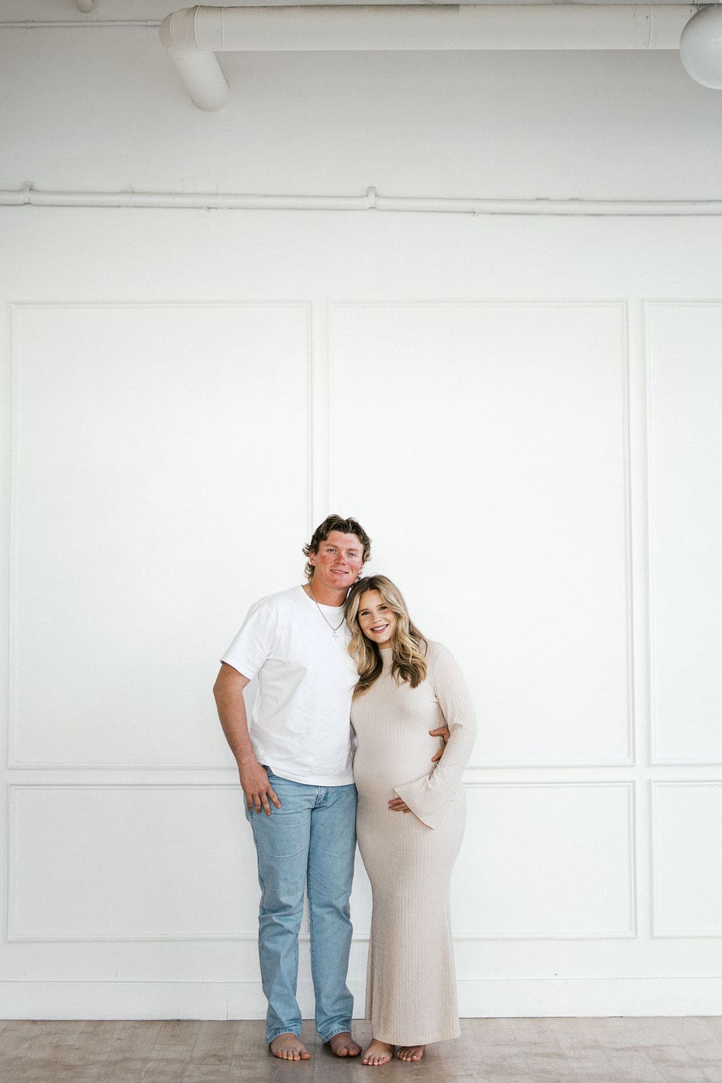A couple holding hands and hugging during their studio materntiy photos as they smile at the camera