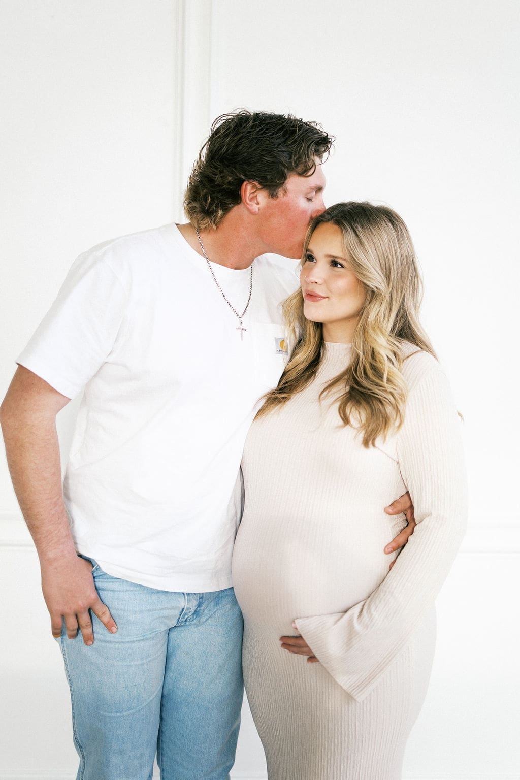 A sweet close photo of the soon to be mom holding her belly as her husband kisses her forehead.