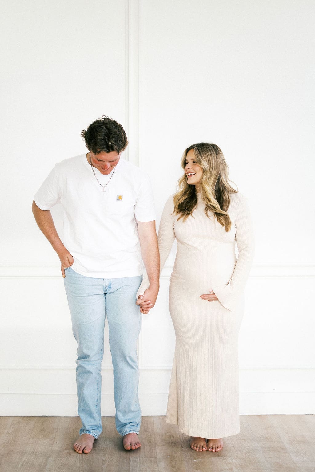 A couple holding hands and laughing candidly during their studio materntiy photos as the mom holds her belly