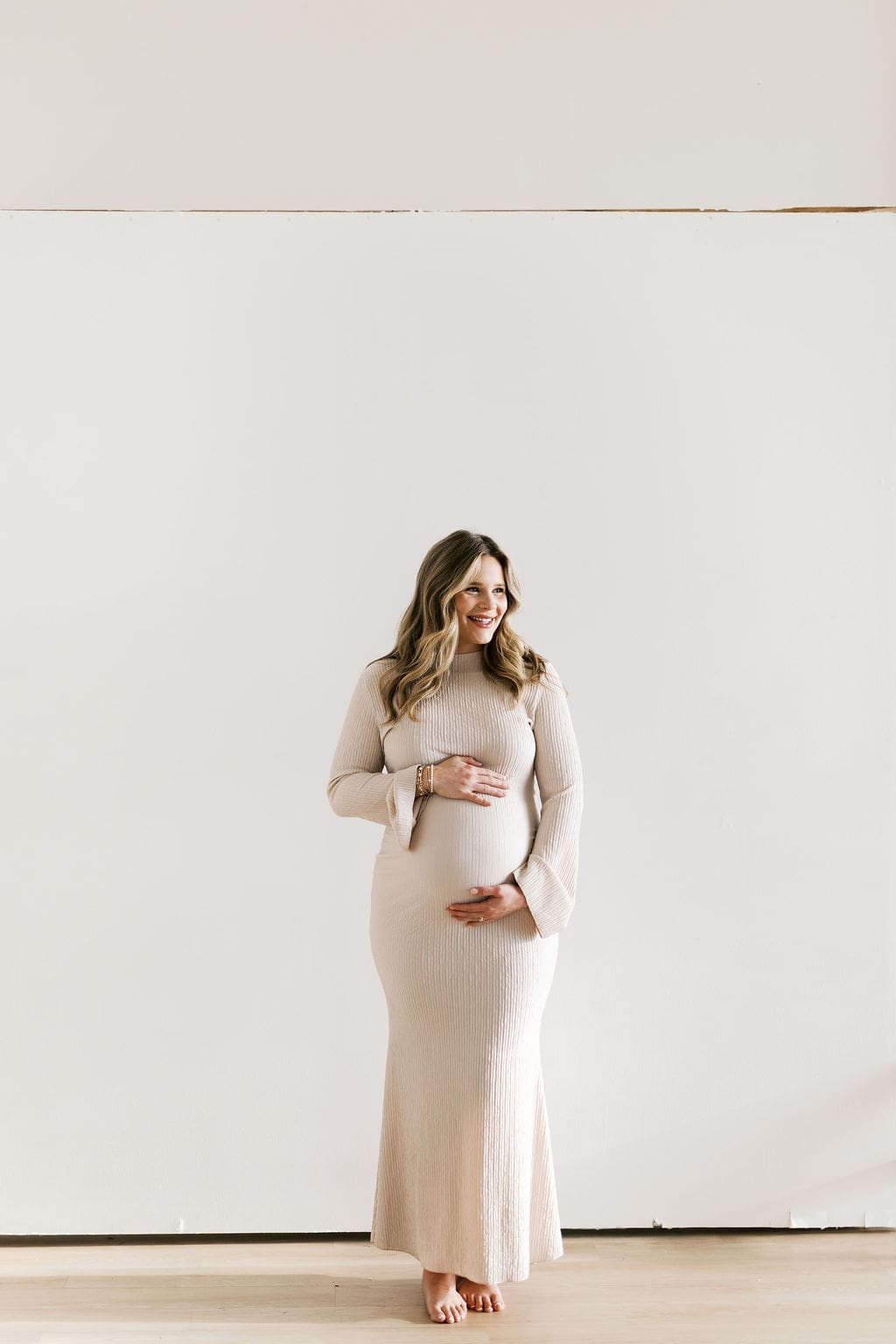 A solo studio maternity photo of the soon-to-be mom holding her belly and looking away from the camera with a soft smile.