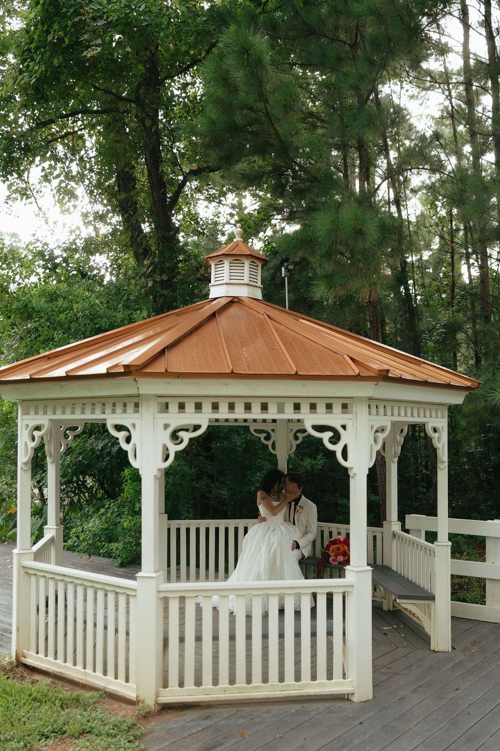 Wide view documentary wedding photos of the bride and groom kissing under a pavillion during their bride and groom portraits.