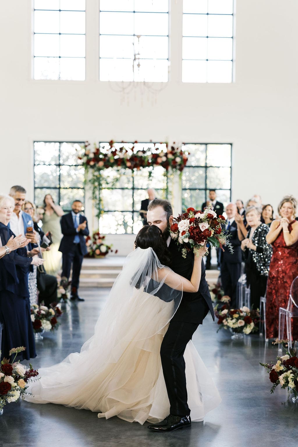 A groom dips his bride for a kiss as they walk back down the aisle at a Persian wedding, surrounded by cheering guests.