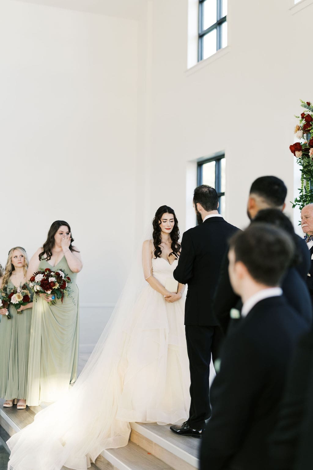 The bride and groom exchange vows at the altar while an emotional bridesmaid wipes tears in the background.