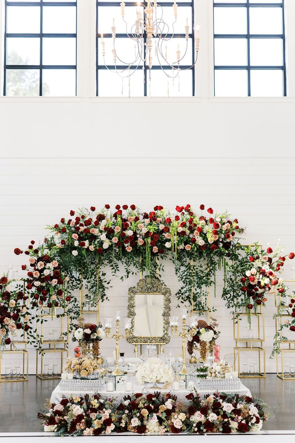 A sofreh aghd ceremony table adorned with a grand floral arch of deep red, blush, and ivory roses at a Persian wedding at Boxwood Manor Houston.