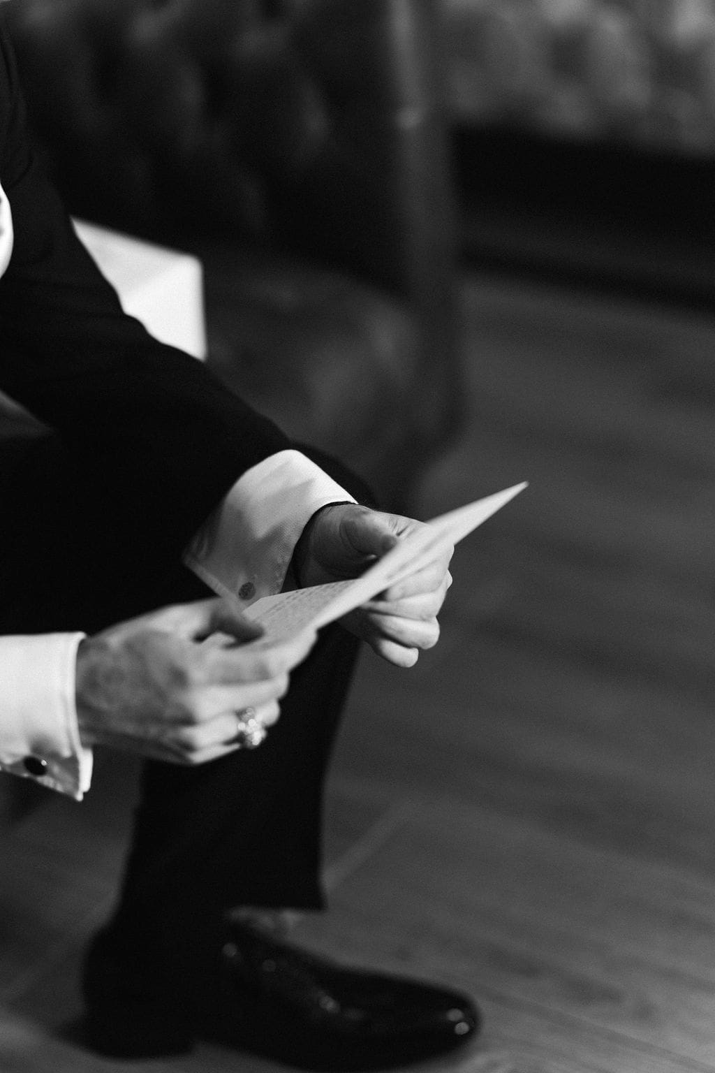 A close-up black and white detail of the groom reading a handwritten letter before the Persian wedding ceremony.