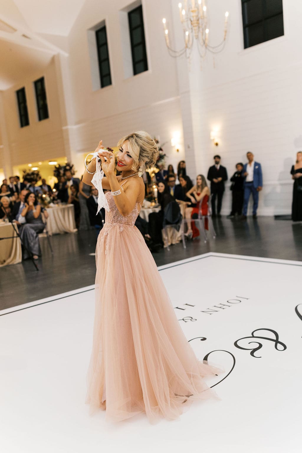 A woman in a blush ballgown twirls on the monogrammed dance floor while holding a floral wrist corsage at the Persian wedding reception.