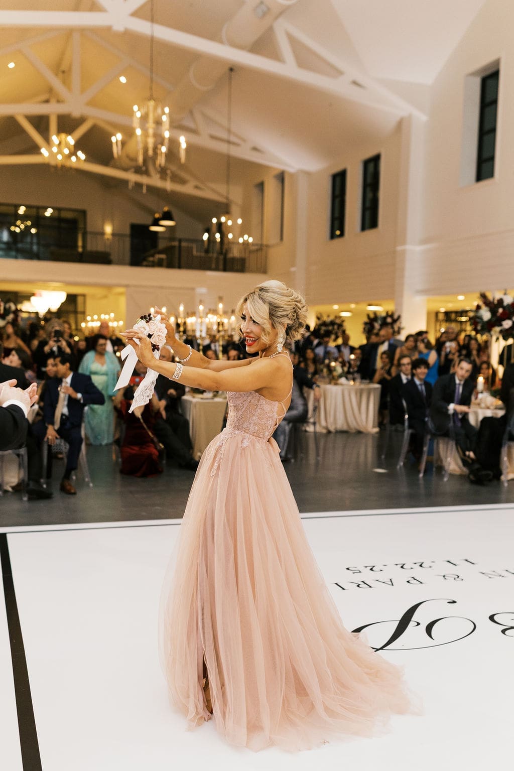 A guest in a flowing blush gown dances on the custom monogrammed dance floor as guests look on during the reception at Boxwood Manor.