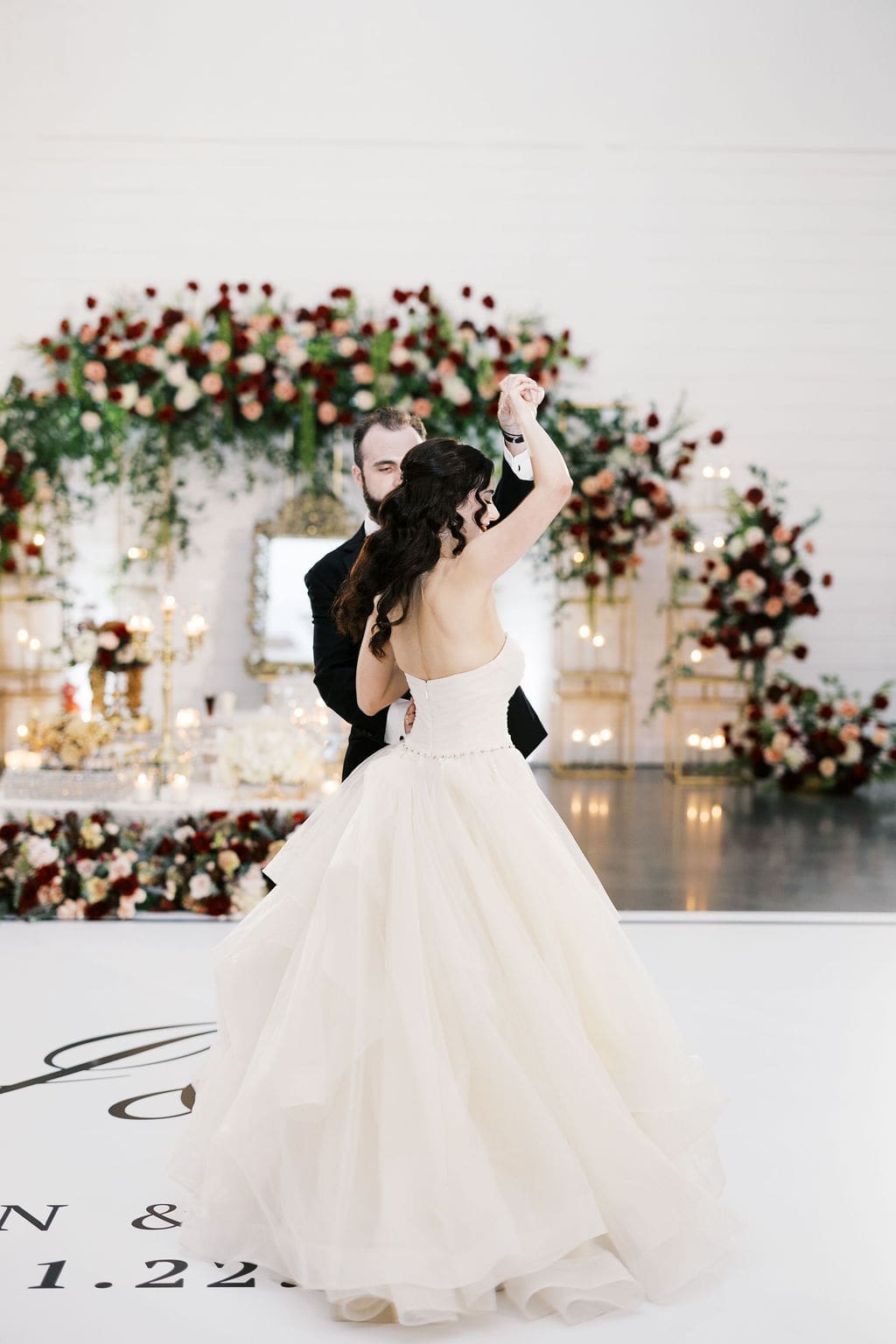 The groom spins his bride in her layered tulle ballgown on the dance floor with the glowing Persian wedding sofreh aghd backdrop behind them.