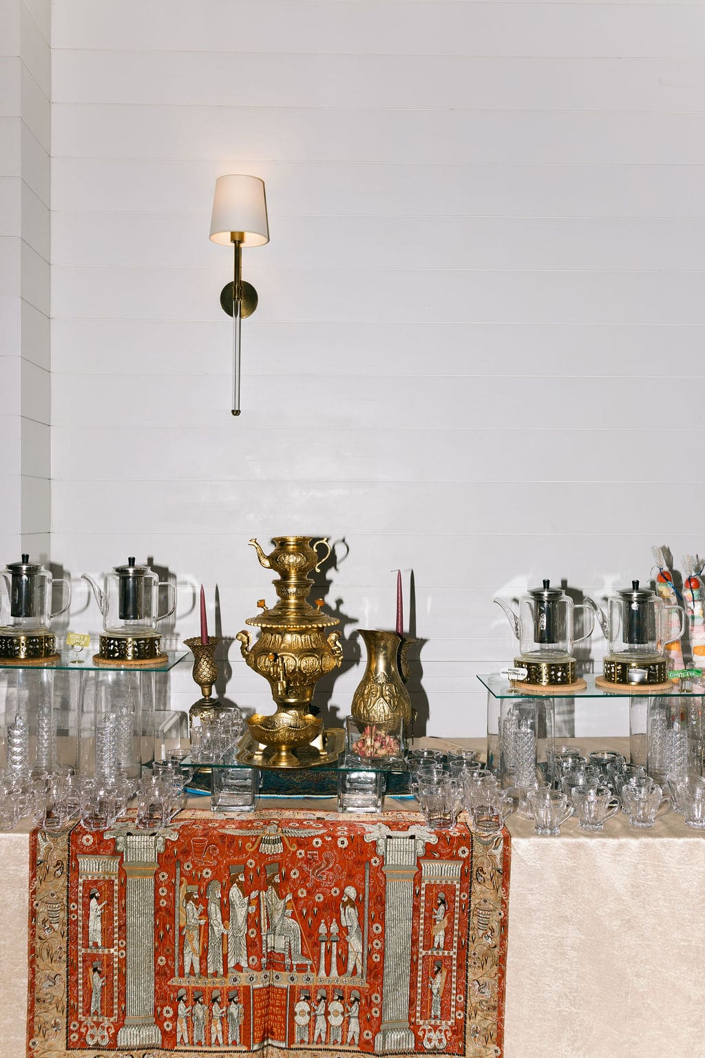 A traditional Persian tea station featuring a brass samovar, ornate carpet runner, and glass teacups arranged on a mirrored surface.